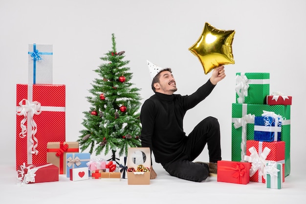 Front view of young man sitting around presents and holding gold star figure on white wall