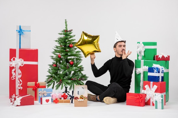 Front view of young man sitting around presents and holding gold star figure on white wall