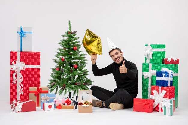 Front view of young man sitting around presents and holding gold star figure on white wall