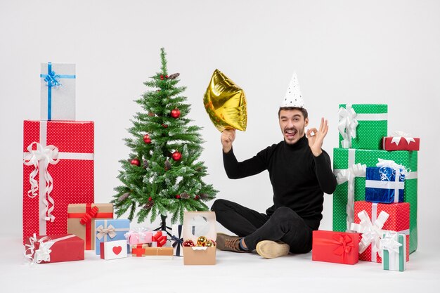 Front view of young man sitting around presents and holding gold star figure on white wall