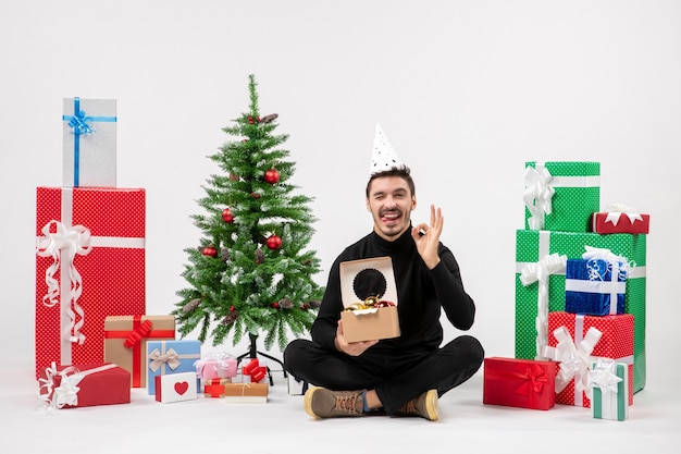 Front view of young man sitting around presents on a white wall