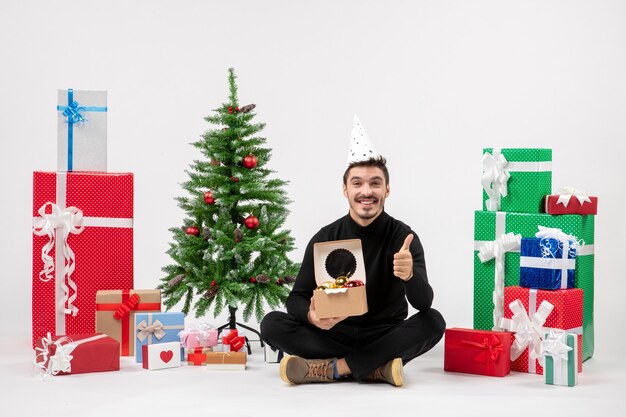 Front view of young man sitting around presents on white wall