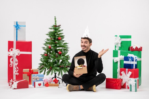 Front view of young man sitting around presents on white wall