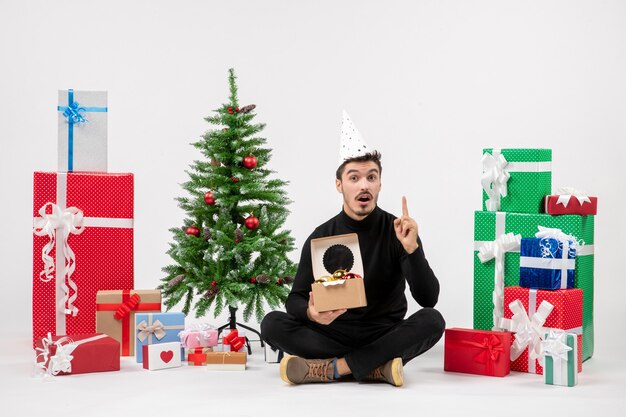 Front view of young man sitting around presents on white wall