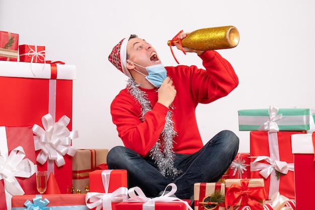 Free photo front view of young man sitting around xmas presents celebrating with champagne on white wall