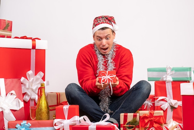 Front view of young man sitting around xmas presents on white wall