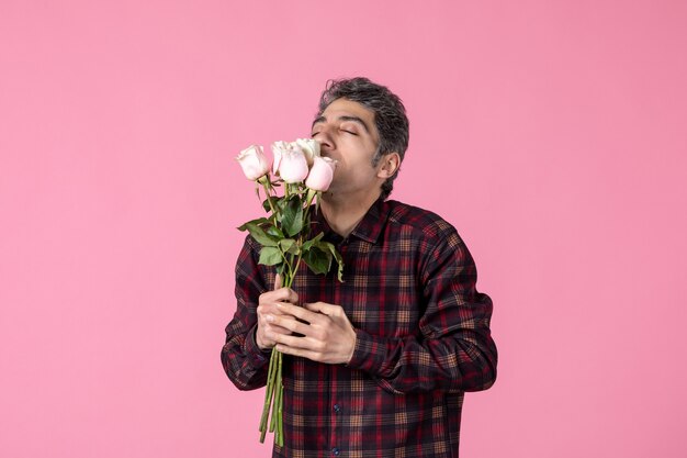 Front view young man smelling beautiful pink roses on pink wall