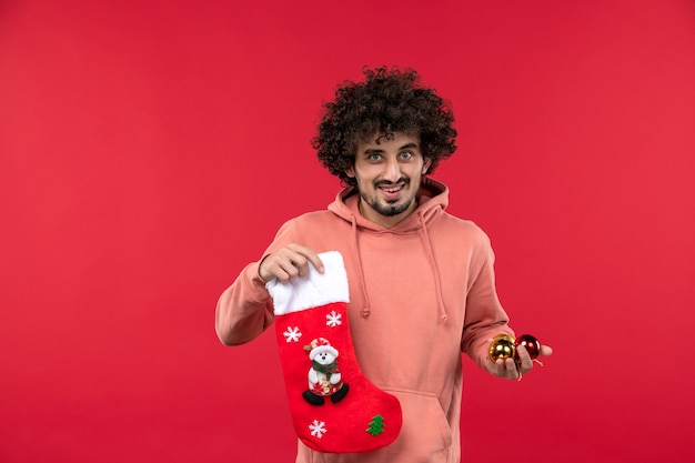 Front view of young man smiling with christmas toys on a red wall