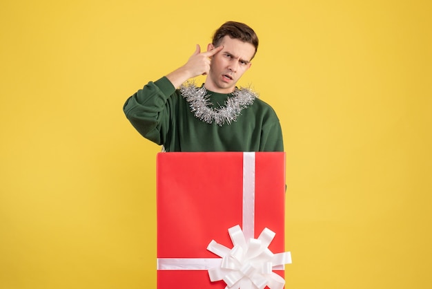 Front view young man standing behind big giftbox on yellow 