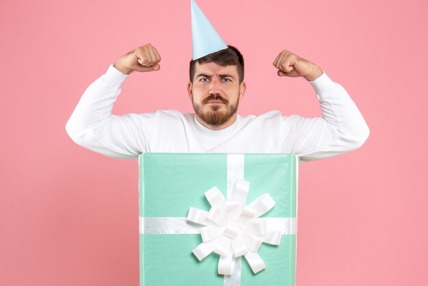 Front view of young man standing inside present box flexing on pink wall