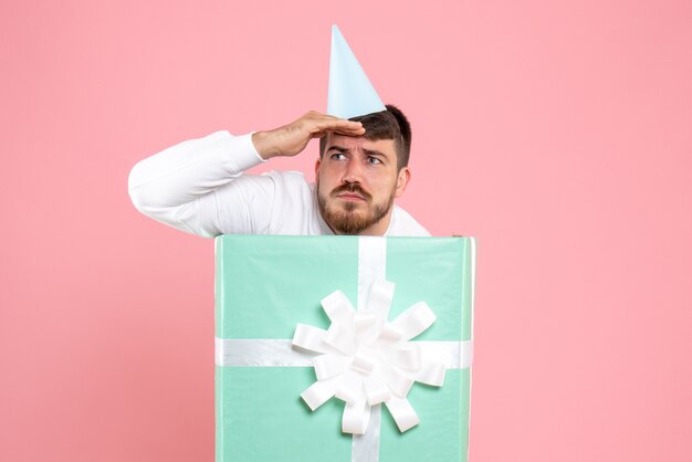 Front view of young man standing inside present box on light pink wall