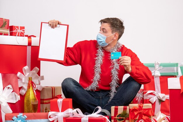 Front view of young man in sterile mask sitting around xmas presents on the white wall