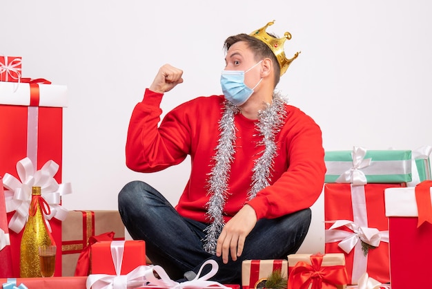 Free photo front view of young man in sterile mask sitting around xmas presents on white wall