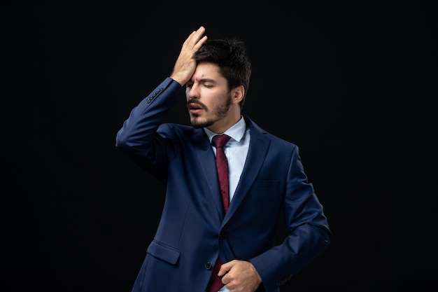 Front view of young man suffering from headache on isolated dark wall