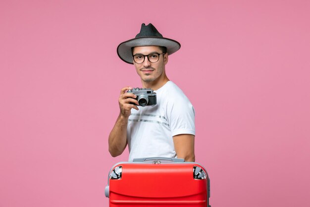 Front view of young man in summer vacation taking photos with camera on the pink wall