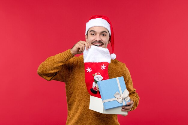 Front view of young man taking christmas sock from box on red wall
