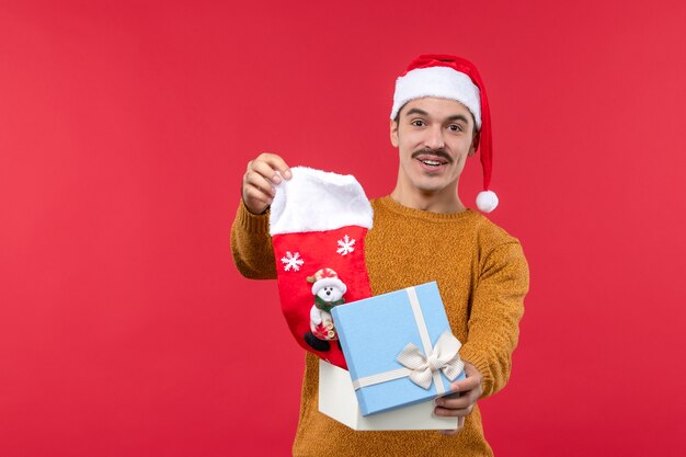 Вид спереди молодого человека, вынимающего рождественский носок на красной стене