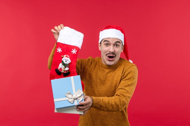 Front view of young man taking out christmas sock on red wall