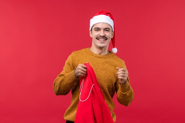 Front view of young man taking out gifts from bag on red wall