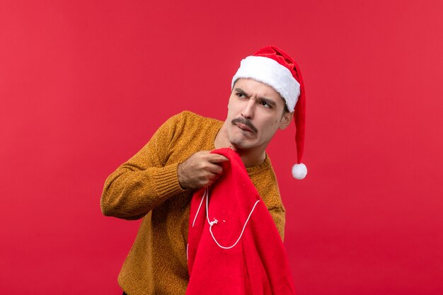 Front view of young man taking out gifts from bag on the red wall