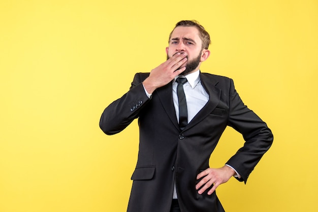 Front view of young man thinking businessman holding hands on mouth on yellow