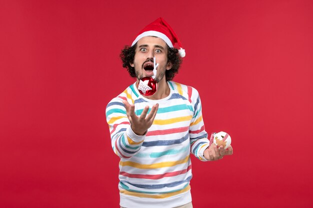 Вид спереди молодой человек бросает елочную игрушку на красную стену праздник красный человеческий новый год