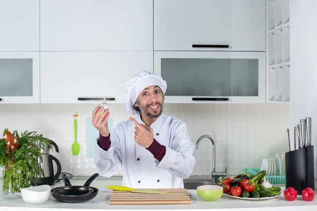 Front view young man in uniform pointing at garlic in kitchen