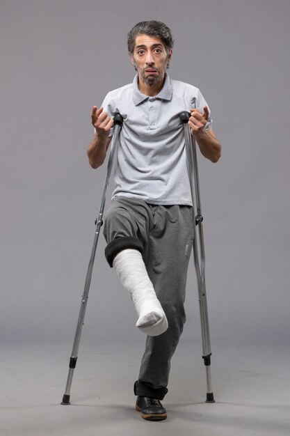 Front view young man using crutches due to broken foot on grey desk disable broken accident leg foot