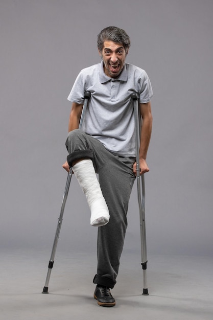 Front view young man using crutches due to broken foot on grey wall disable broke broken accident legs foot