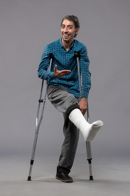 無料写真 灰色の壁の脚の事故で足が折れたために松葉杖を使用している正面図の若い男は壊れた損傷を無効にします