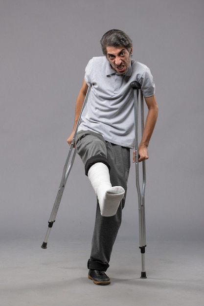 無料写真 灰色の床の壊れた足のために松葉杖を使用している正面図の若い男は壊れた事故の足の足を無効にします
