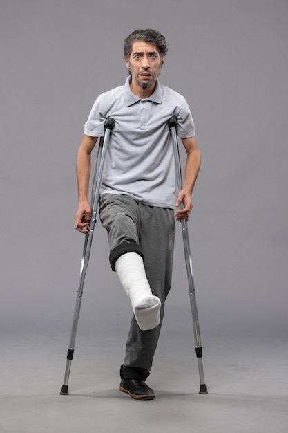 無料写真 灰色の壁の事故で足が折れたために松葉杖を使用している正面図の若い男が壊れた足の損傷を無効にする