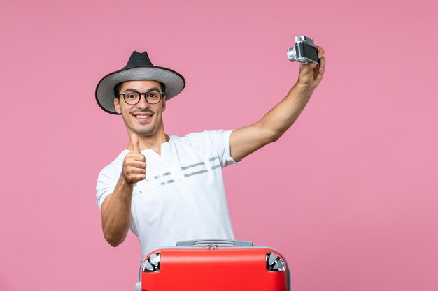 밝은 분홍색 벽에 사진을 찍는 카메라를 들고 가방을 들고 휴가 중인 젊은 남자의 전면 보기