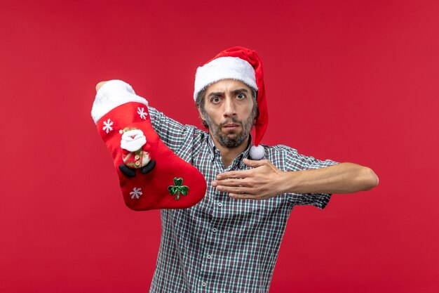 Front view of young man wearing christmas sock on red wall