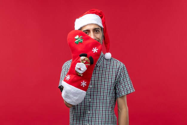 Вид спереди молодого человека в рождественском носке на красной стене