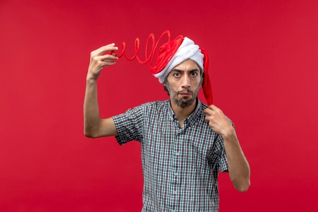 Front view of young man wearing funny toy cap on red wall