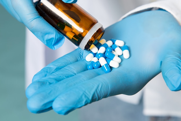 A front view young man in white shirt and blue gloves taking pills on the blue space