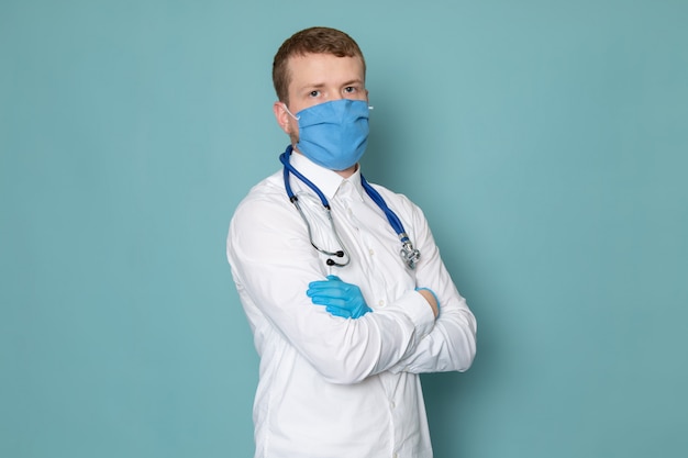 A front view young man in white shirt and blue gloves with blue mask on the blue space