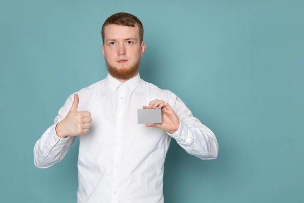 A front view young man in white shirt holding card on the blue space