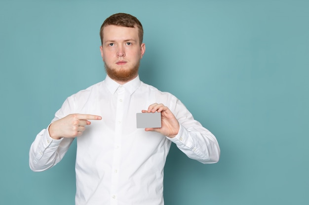 A front view young man in white shirt holding card on the blue space