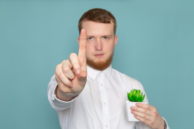 青いスペースに小さな緑の植物を保持している白いシャツの正面の若い男