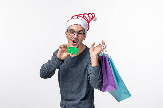 Front view of young man with bank card and packages on the white wall