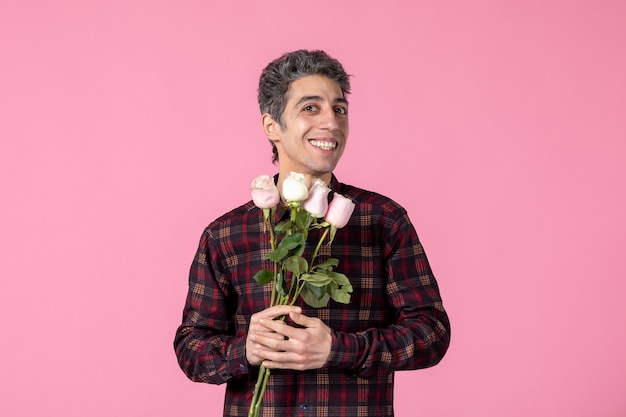 Front view young man with beautiful pink roses on pink wall