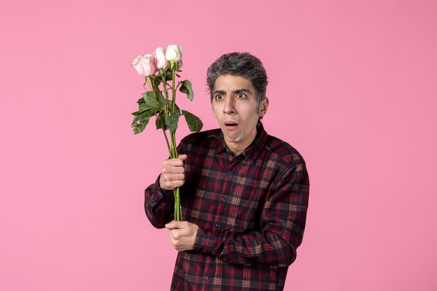 Front view young man with beautiful pink roses on pink wall