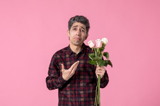 Front view young man with beautiful pink roses sad on pink wall