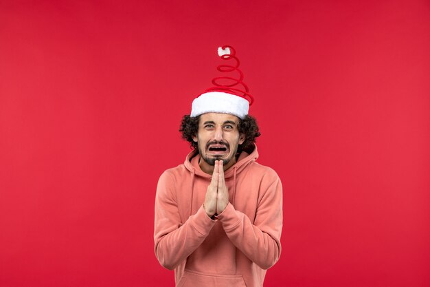 Front view of young man with begging expression on red wall