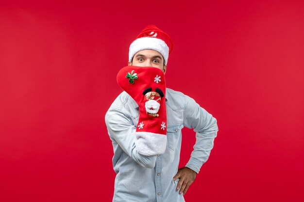 Вид спереди молодого человека с большим рождественским носком на красной стене