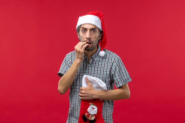 Front view of young man with big christmas sock on red wall