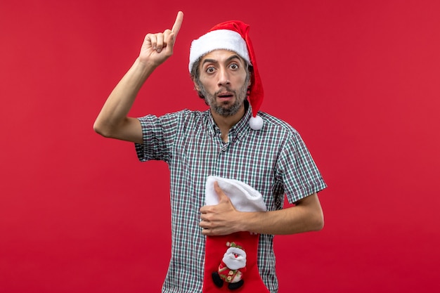 Front view of young man with big christmas sock on the red wall