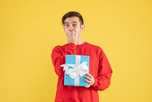 Front view young man with blue giftbox standing on yellow 